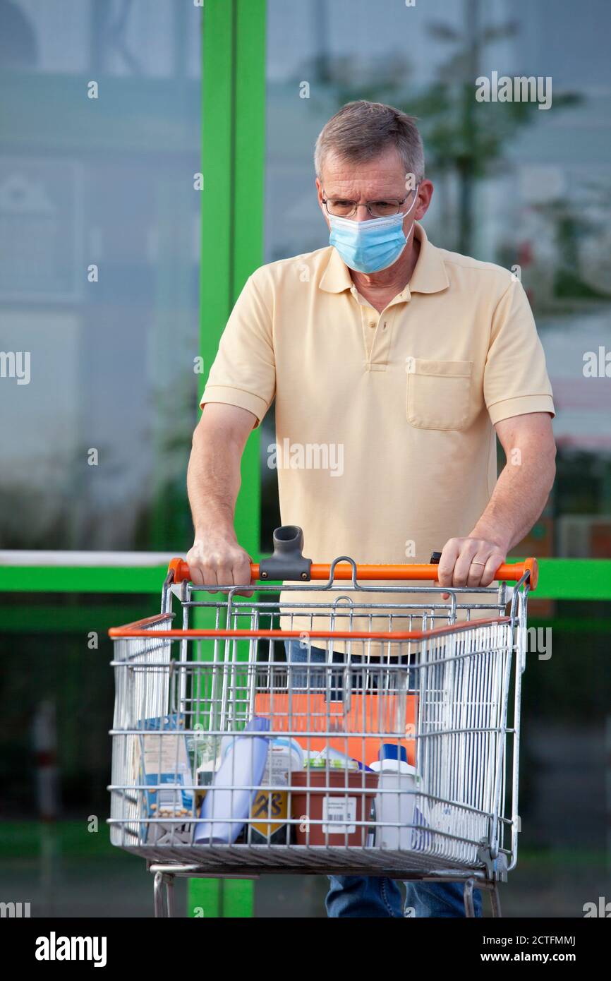 Sad old man with face mask leaving a super market with a shopping cart - focus on the head Stock Photo