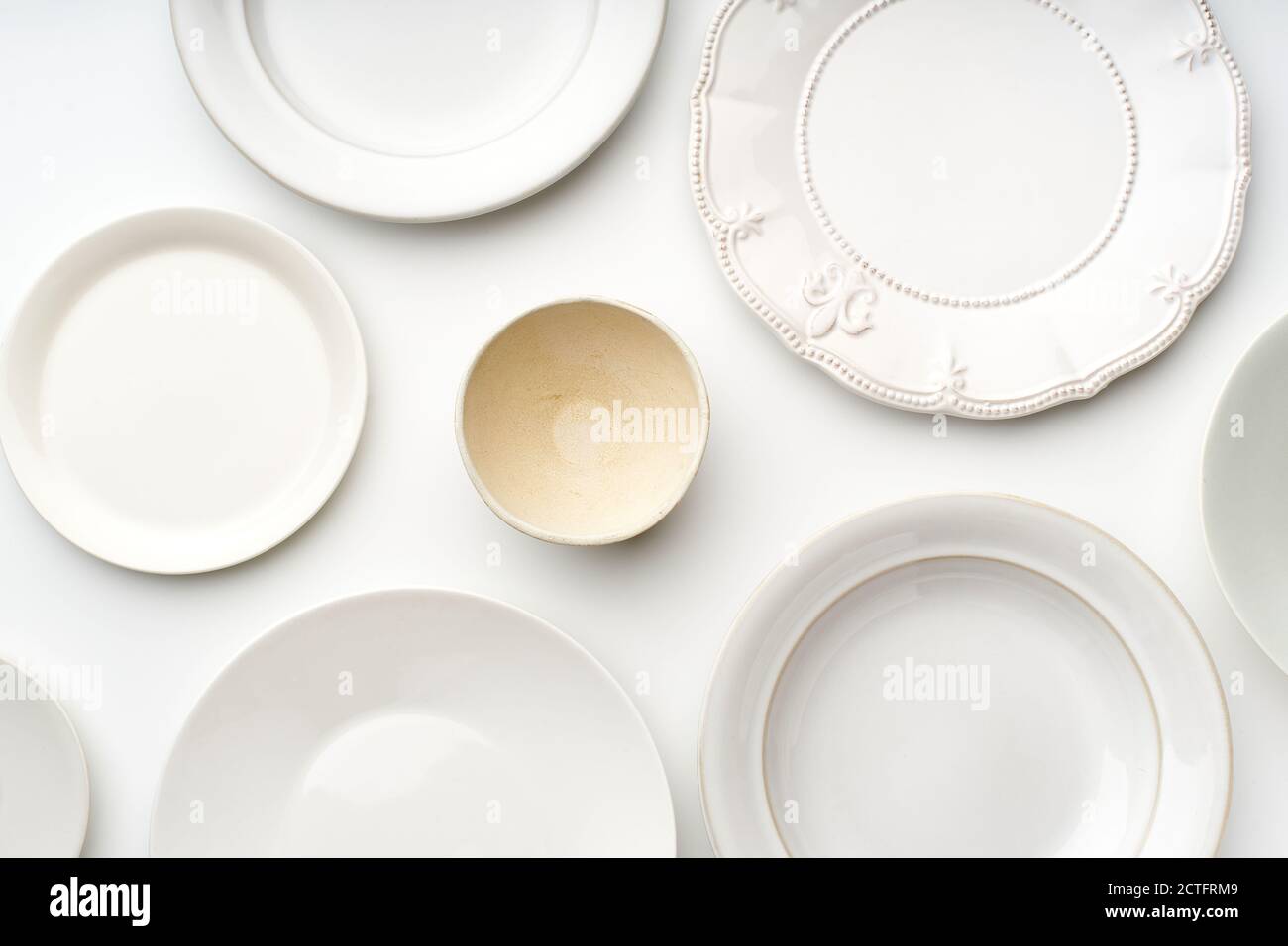 Flat lay with many white ceramic plates of various shapes and sizes. Kitchen tableware top view