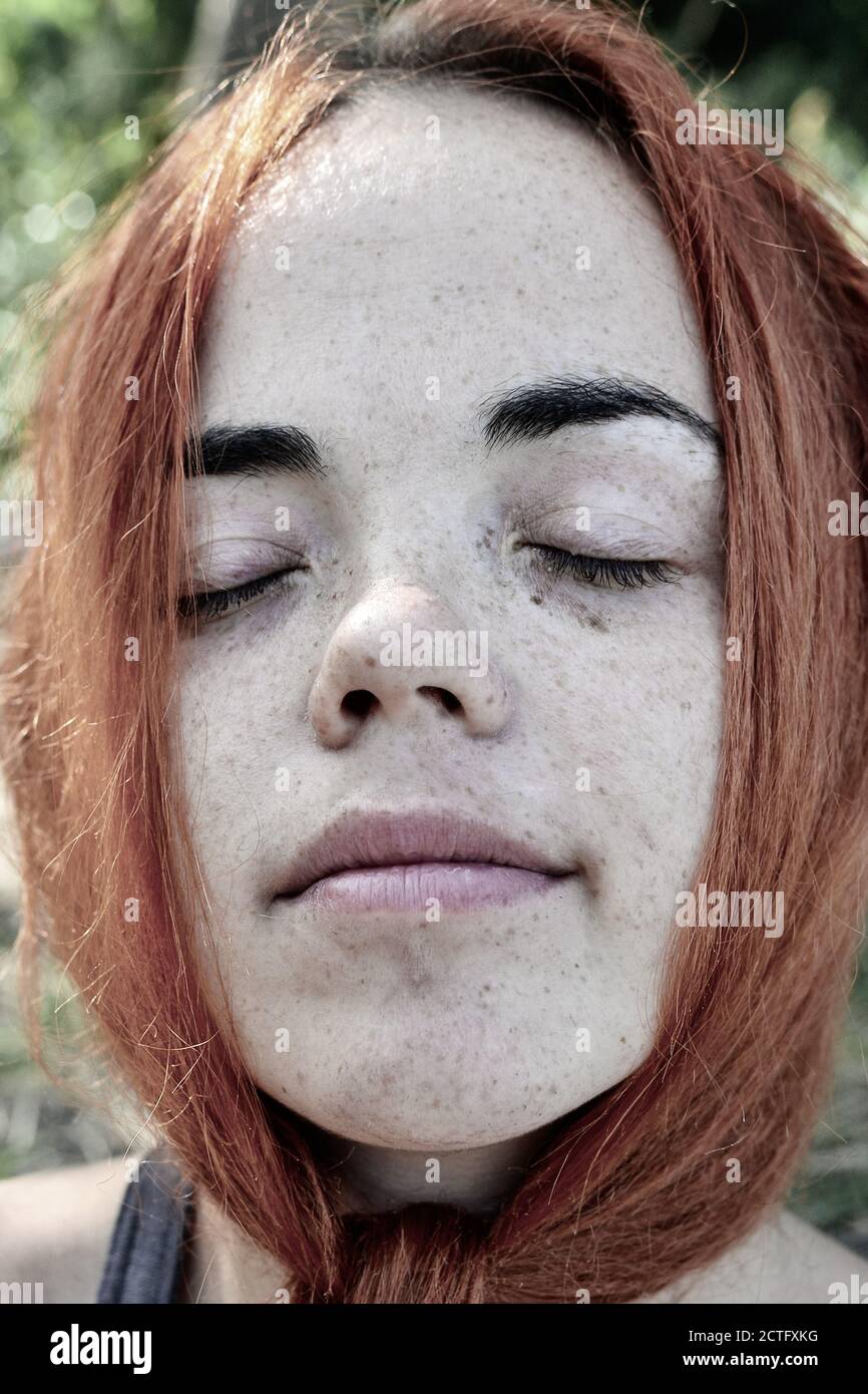 Close up portrait of a red hair woman girl with freckles. Portrait of a girl outdoors in sunlight. Closed eyes Stock Photo