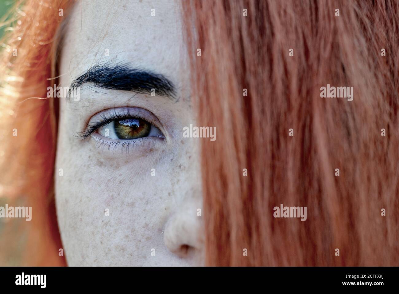 Close up portrait of a red hair woman girl with freckles. Portrait of a girl outdoors in sunlight. Hair covers half of the face. Stock Photo