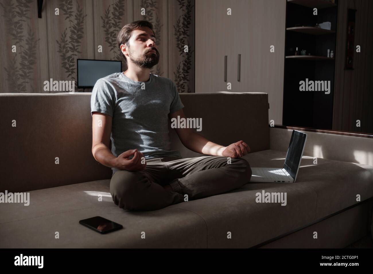 millennial hipster guy enjoy no stress peace of mind lounge on sofa at home. Men do meditation with laptop and phone on sofa Stock Photo