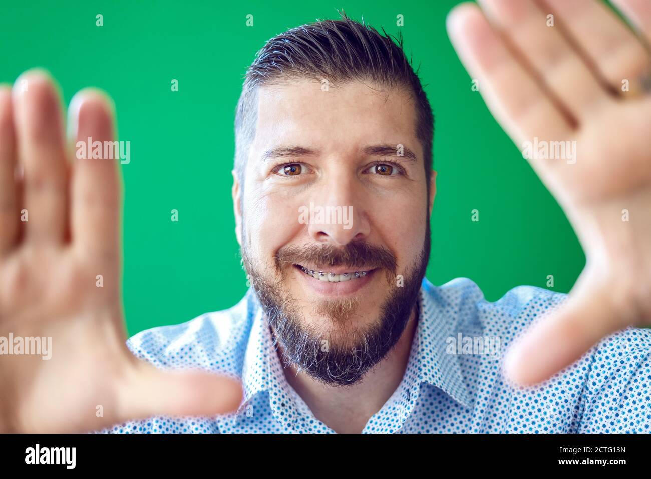 Mature bearded man with braces having fun making a frame with hands Stock Photo