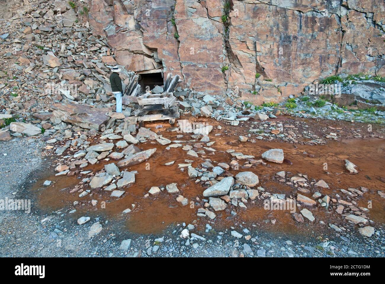 Man at adit entrance to underground gold mine, rust colored water coming out of tunnel, road to Clear Lake, San Juan Mountains, Colorado, USA Stock Photo