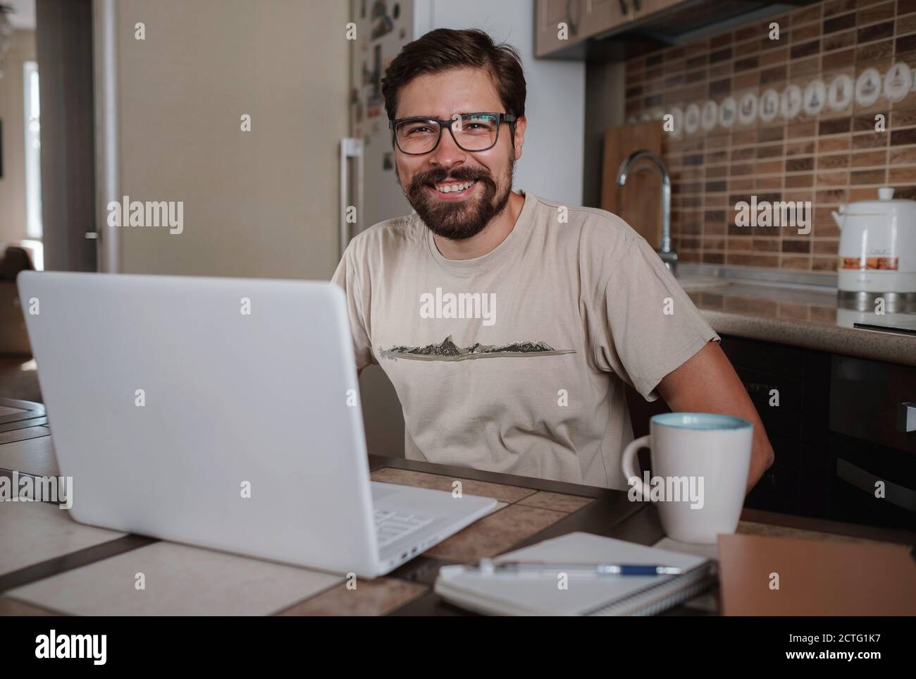Satisfied with work done. Happy young man working on laptop while sitting at his working place in home office. Happy employee feeling no stress, relax Stock Photo