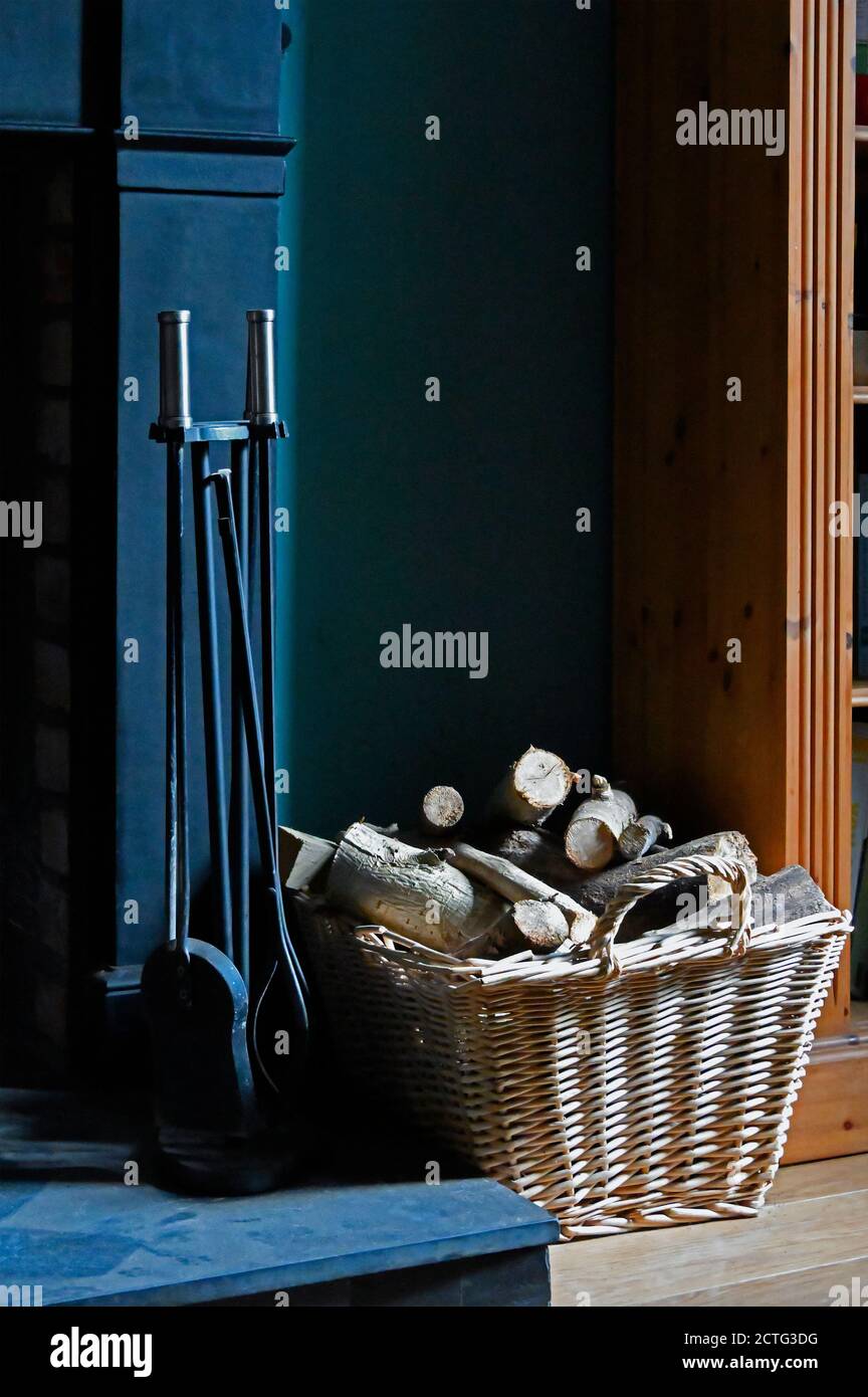 Fire irons and firewood in basket on hearth. Stock Photo