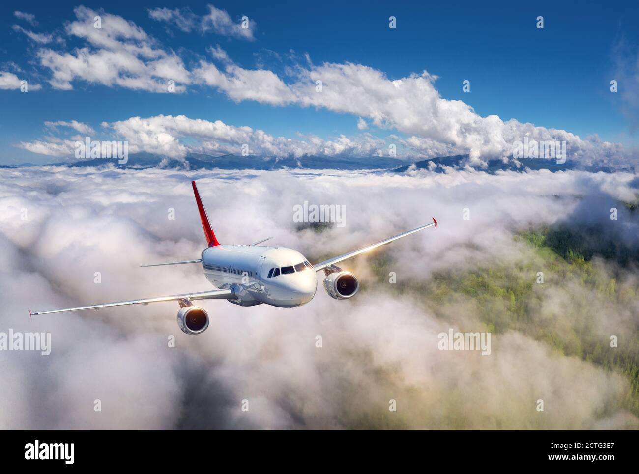Airplane is flying in low clouds over mountains at sunset Stock Photo