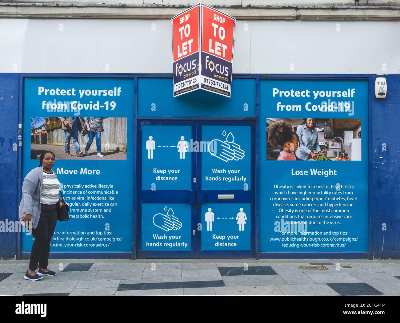 A women stands in front of a large public health poster in Slough, reminding people how to protect themselves from Covid. Stock Photo