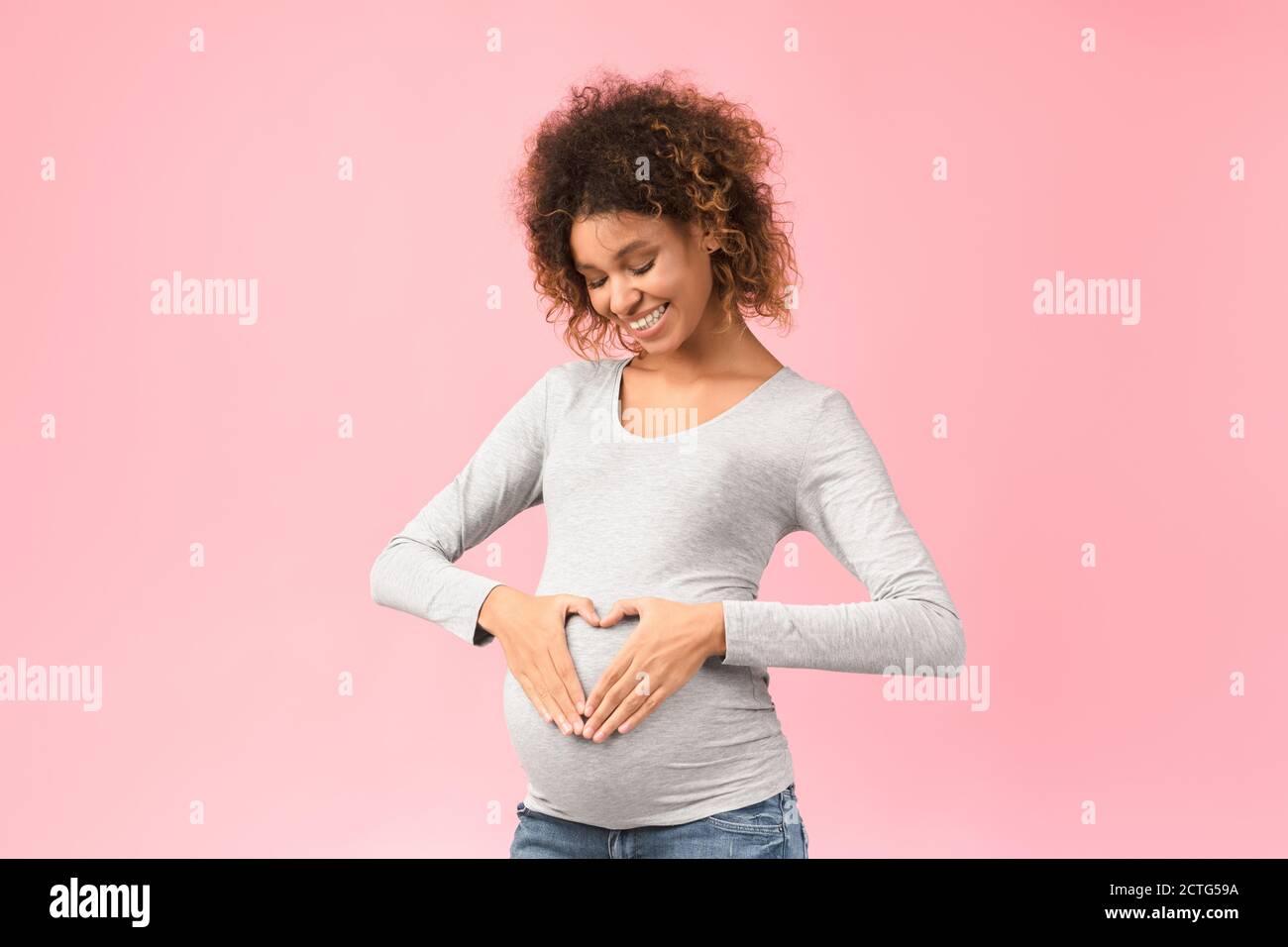 Happy expectation. Afro woman making heart shape on pregnant belly