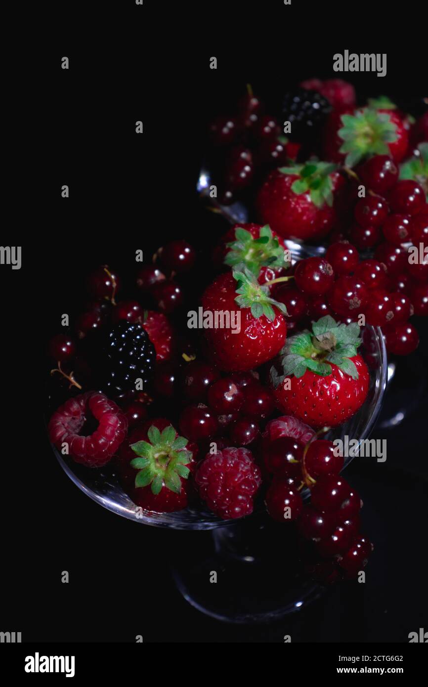 Different red fruits in a glass reflecting in a mirror, strawberries, berries Stock Photo