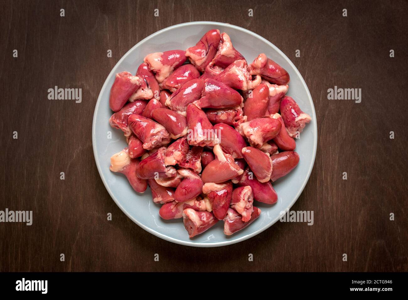 Raw fresh chicken hearts in gray plate isolated on wooden background top view Flat lay Offal ready for cooking Healthy food Stock Photo