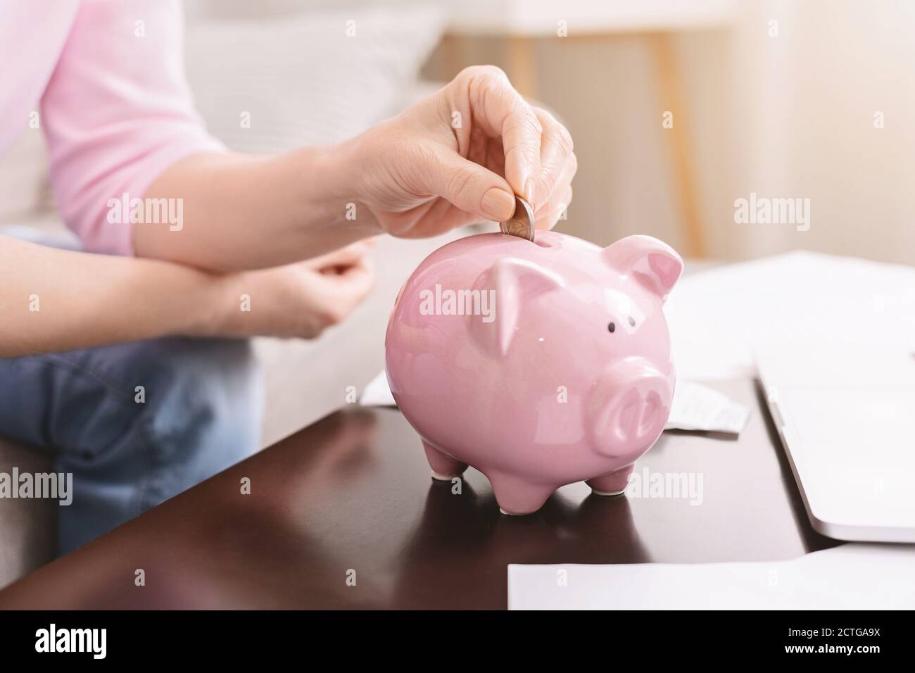 Senior lady putting coins into pink piggy bank Stock Photo - Alamy