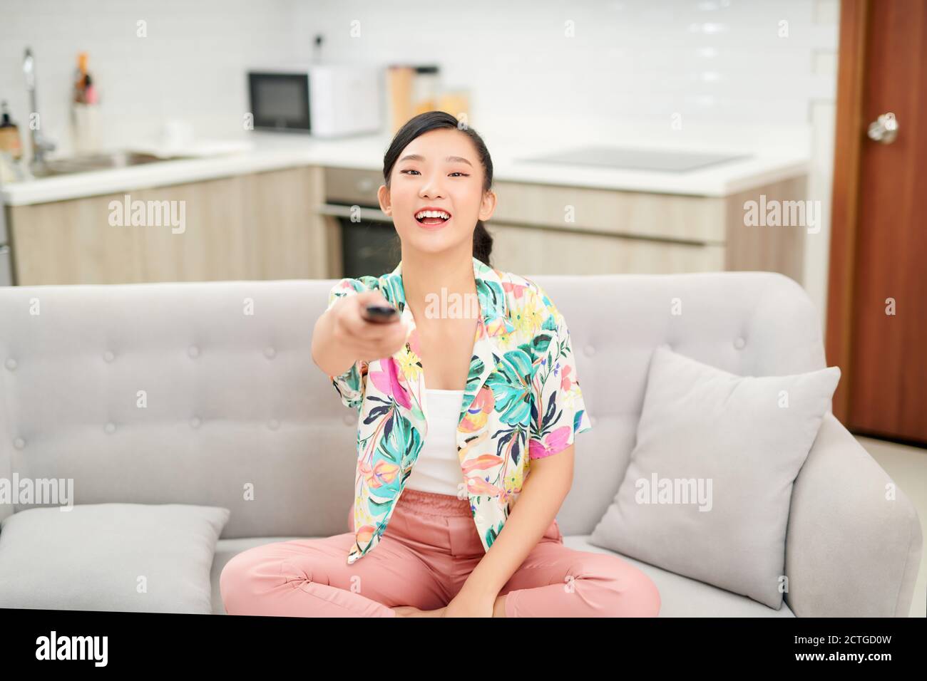 television, relax, home and happiness concept - smiling teenage girl sitting on couch with tv remote control at home Stock Photo
