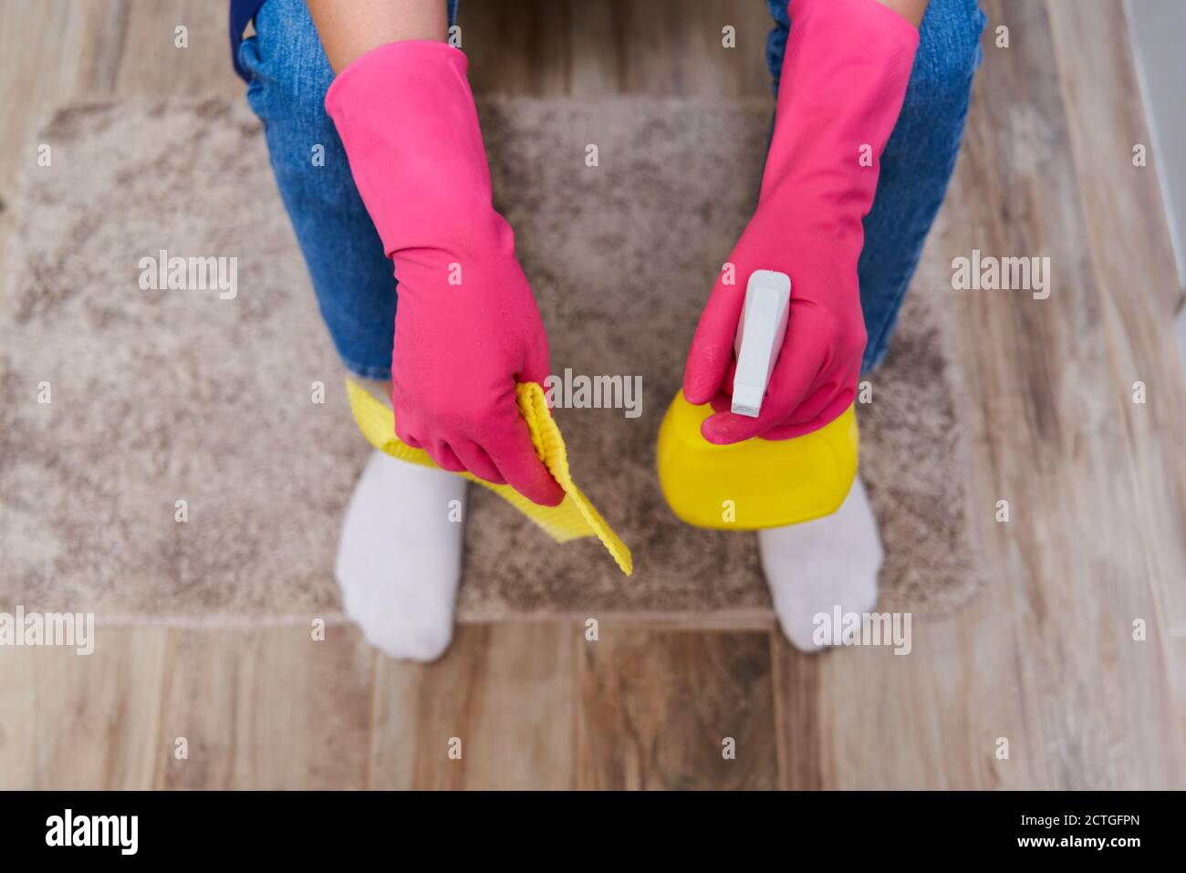 Tired woman in rubber gloves sitting on a toilet and holding cleaning spray. Top view Stock Photo