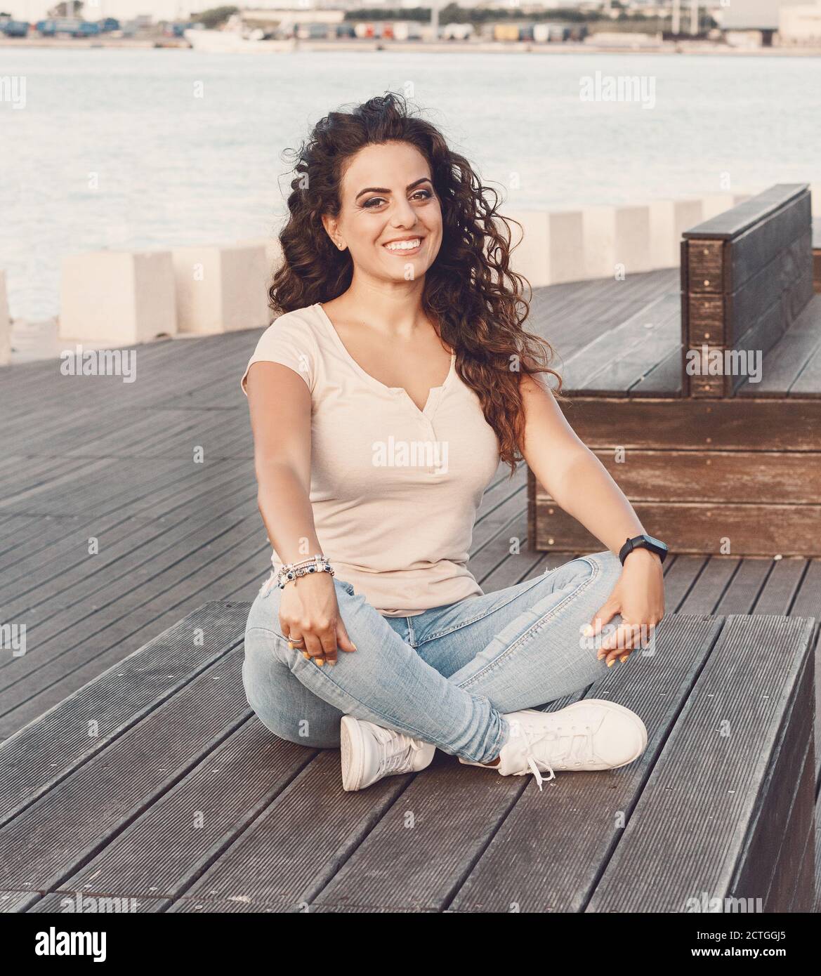 Young women wearing t-shirt and jeans sits on the wooden  bench and smile Stock Photo