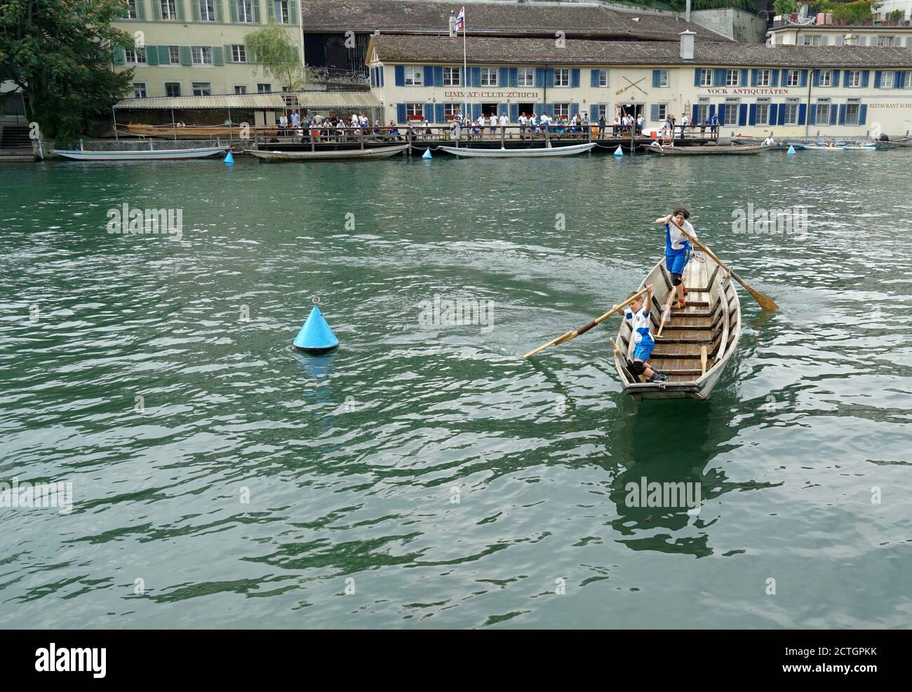 A Swiss fisherman traditional wooden boat with one small boy and woman. They are standing and move the vessel with oars on the Limmat river in Zurich. Stock Photo