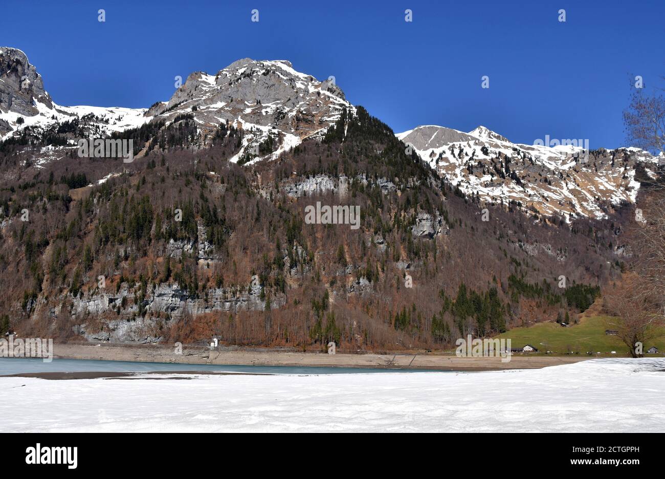 Panorama of Alps from Klontalersee lake in the foreground in early spring sunny day in Klöntal, Schwyz Alps, canton Glarus, Switzerland. Steep slopes. Stock Photo
