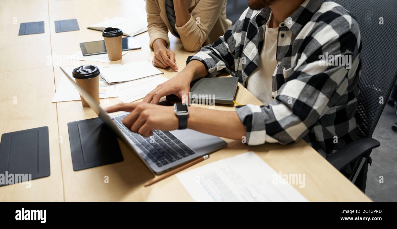 Cropped shot of a male office worker using laptop and discussing project with his colleague while working together in the office. Business people and technology, teamwork Stock Photo