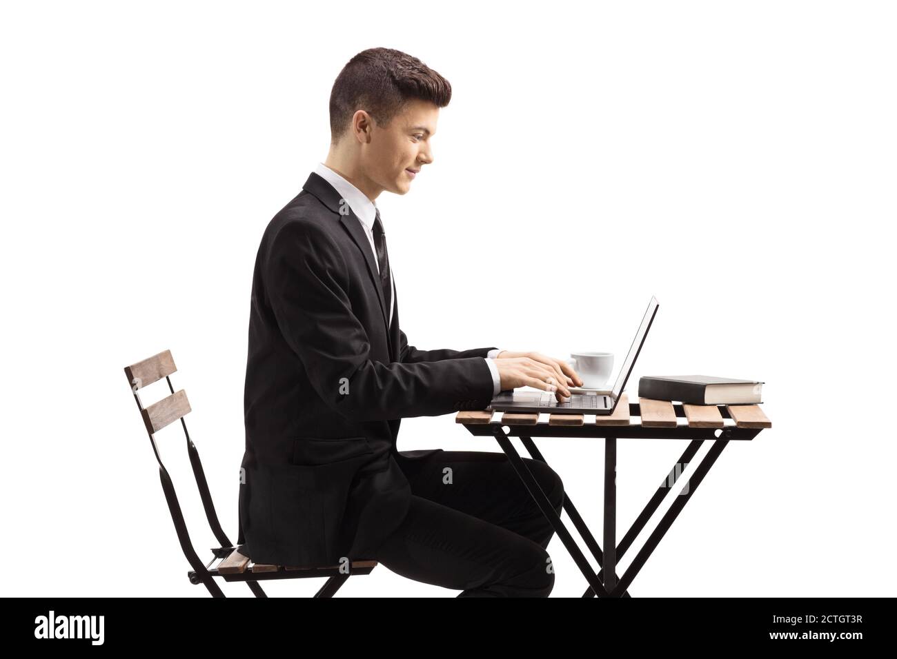 Guy in a suit sitting at a coffee table and working on a laptop isolated on white background Stock Photo