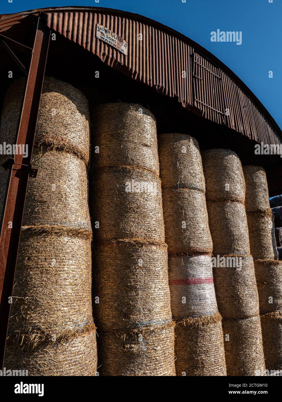 A rusty corrugated sheet metal dutch barn containing large round straw