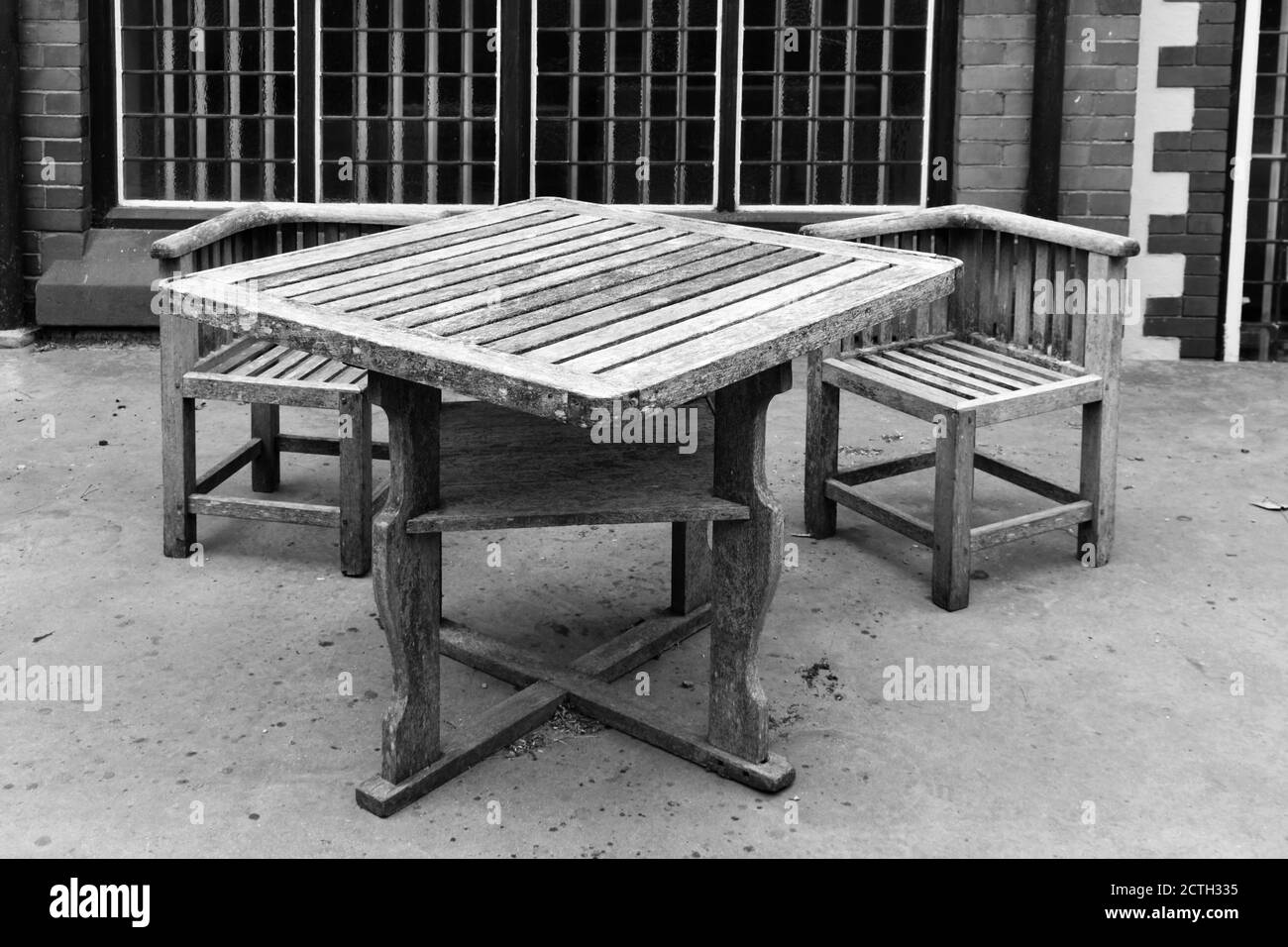 black and white image of Isolated rustic wooden table and chairs outside building on concrete patio in summer Stock Photo