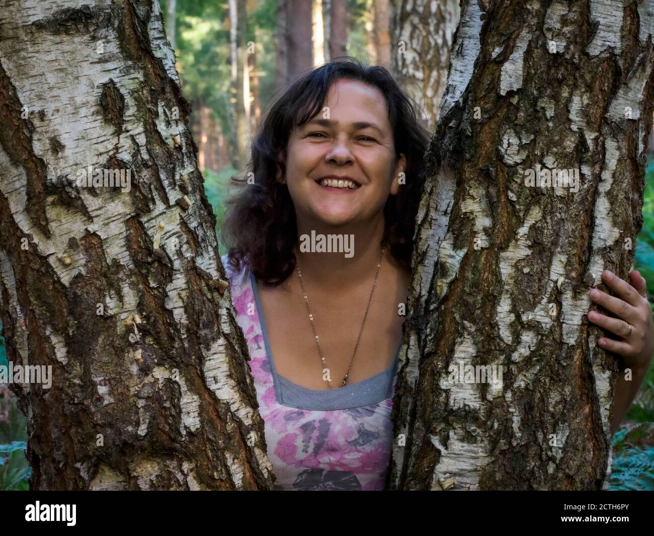 Middle aged woman posing between tree trunks, UK Stock Photo