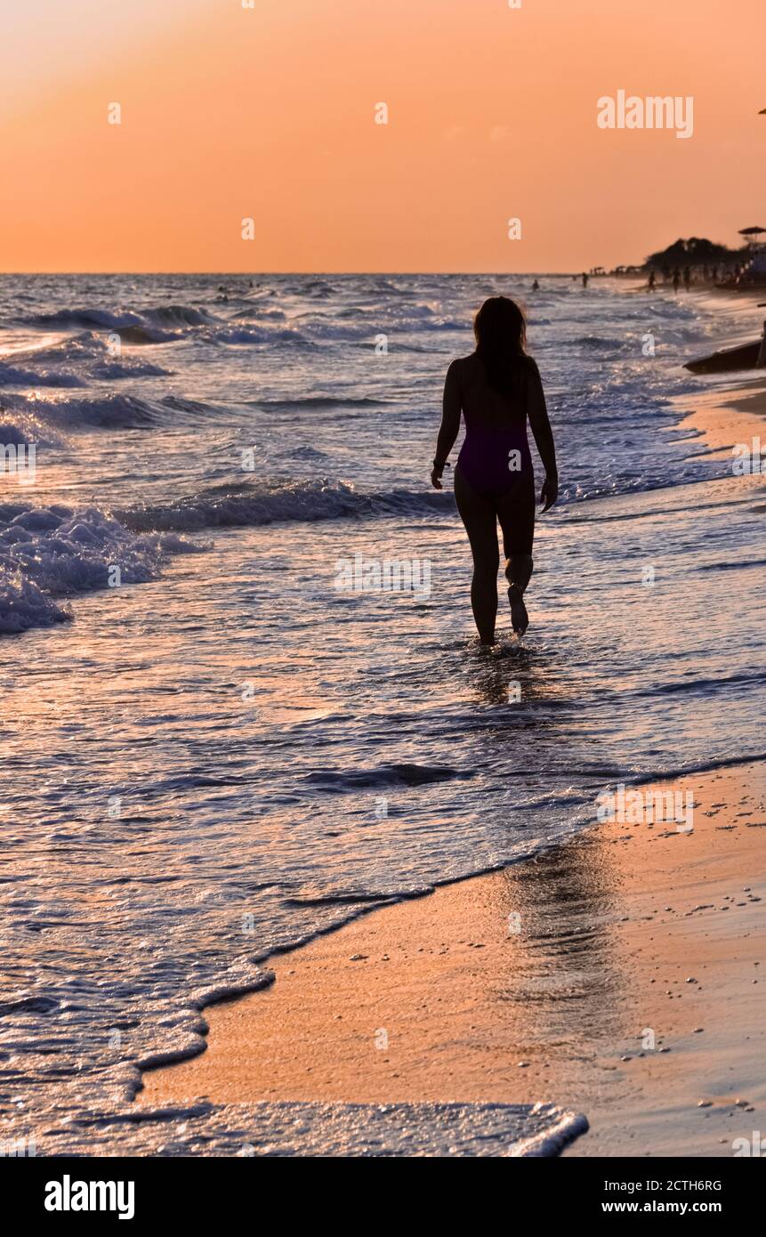 Summertime: girl walking on the shore at sunset among the waves. Stock Photo