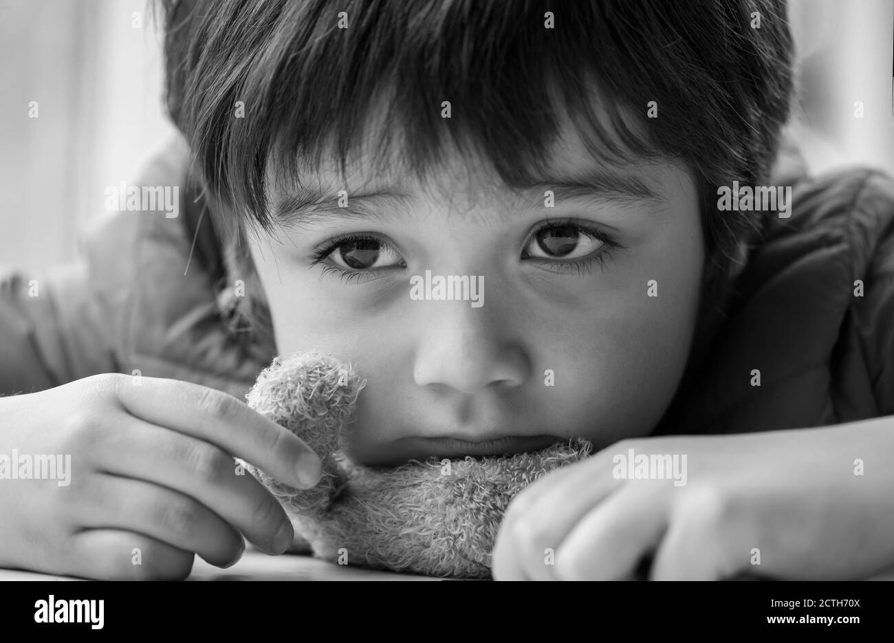 Black and white photo of Kid with bored face,Lonely boy putting his chin down on teddy bear and looking out, Upset preschool child with unhappy or sad Stock Photo