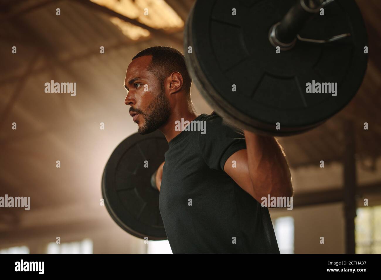 Man exercising with barbell. Male bodybuilder doing weight lifting workout at cross training gym. Stock Photo