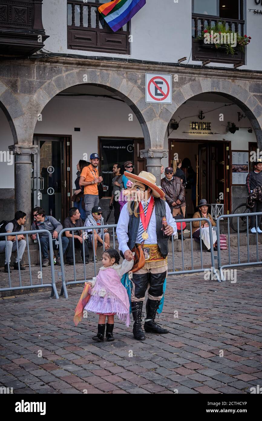 A pretty young girl holds hands with an adult in fancy dress and a mask during the Inti Raymi'rata sun festival over the winter solstice, Cusco, Peru Stock Photo