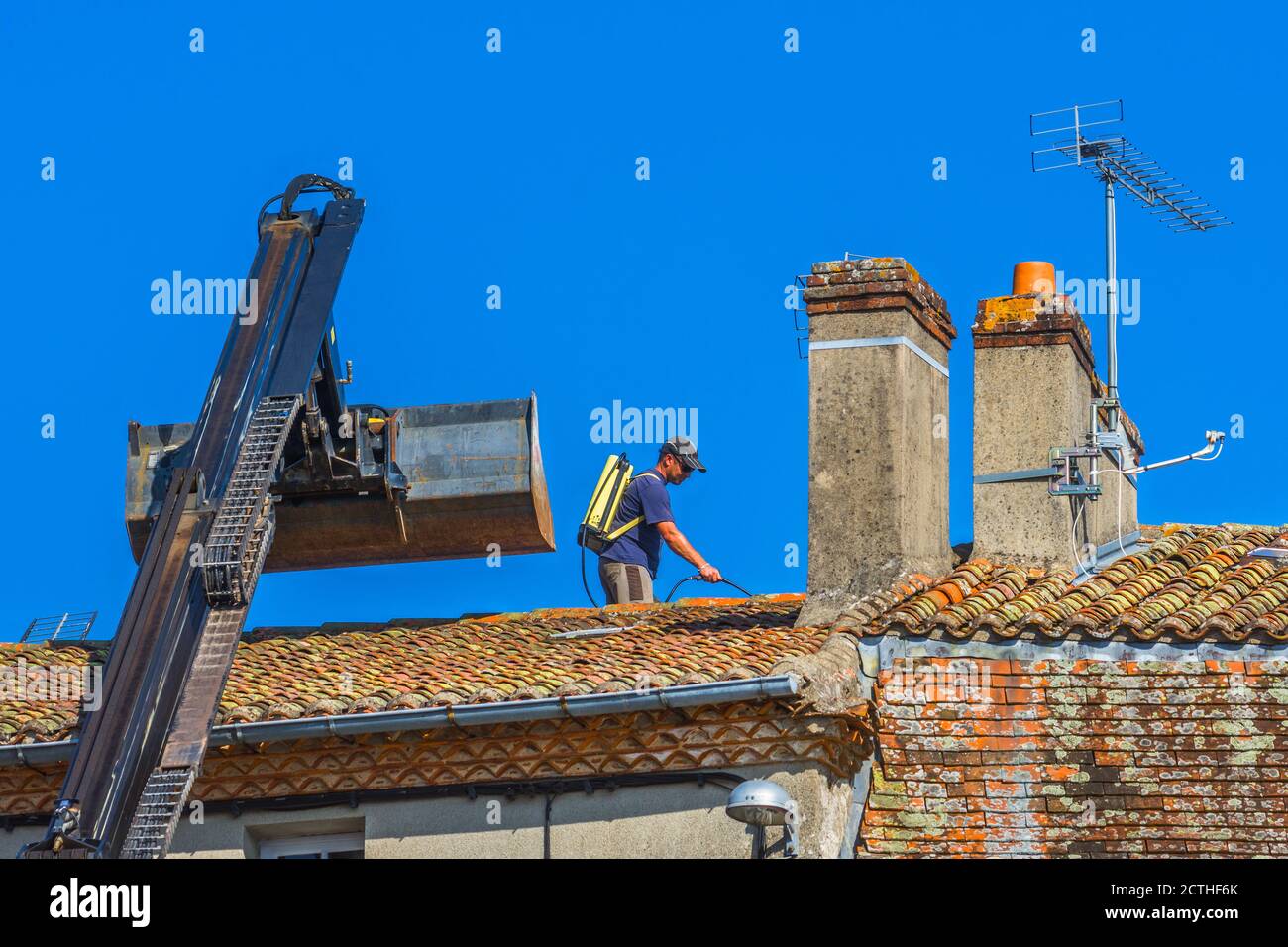 Worked spraying moss on pantile roof - Le Dorat, Haute-Vienne (87), France. Stock Photo