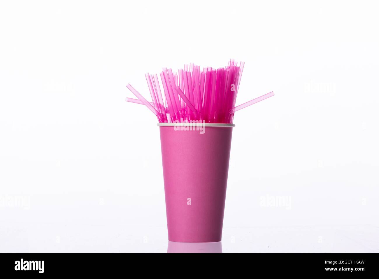 Bunch of pink plastic straws in pink biodegradable paper cup isolated