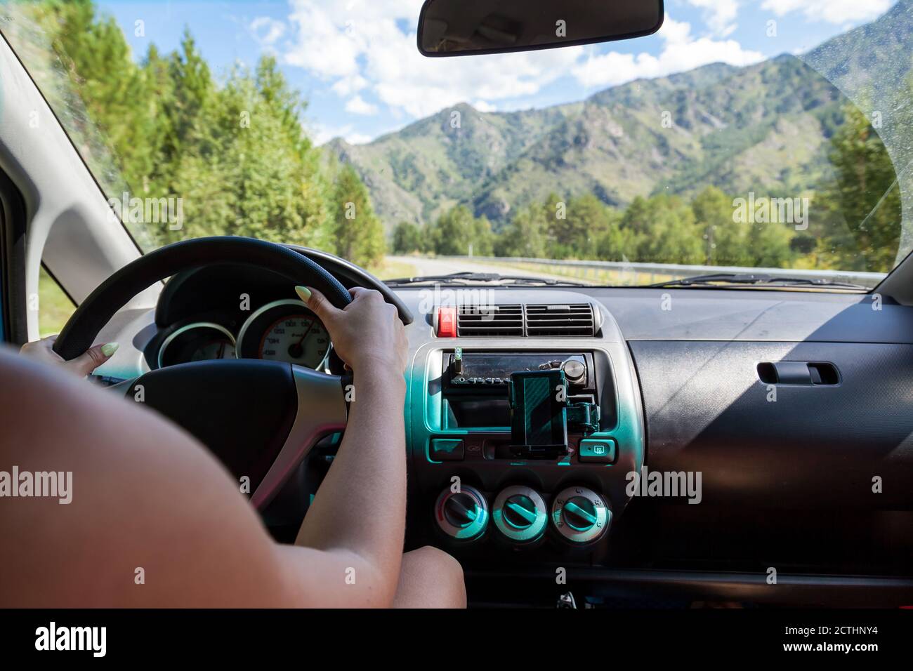 Women's hands behind the wheel of a Japanese Honda car with a view of the mountain ranges through the windshield and the serpentine road. Stock Photo