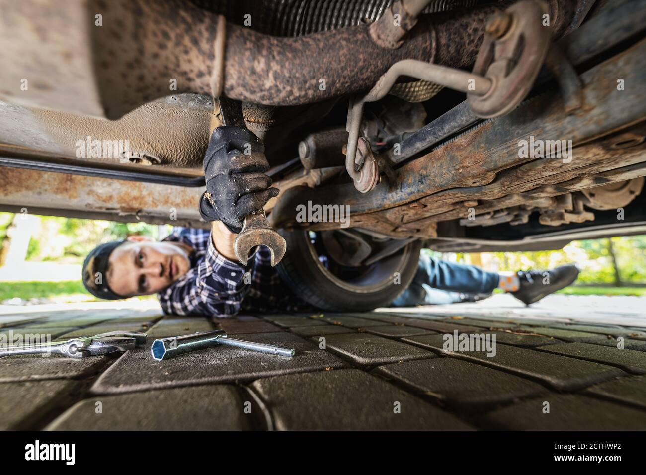 man laying on the ground under the car and repairing engine with wrench Stock Photo