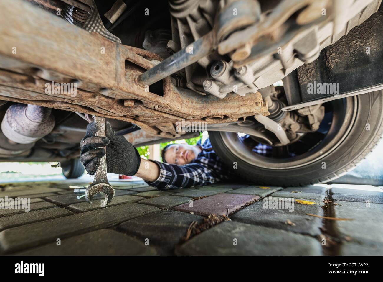 man repairing car. mechanic inspecting suspension system under the vehicle at home garage Stock Photo