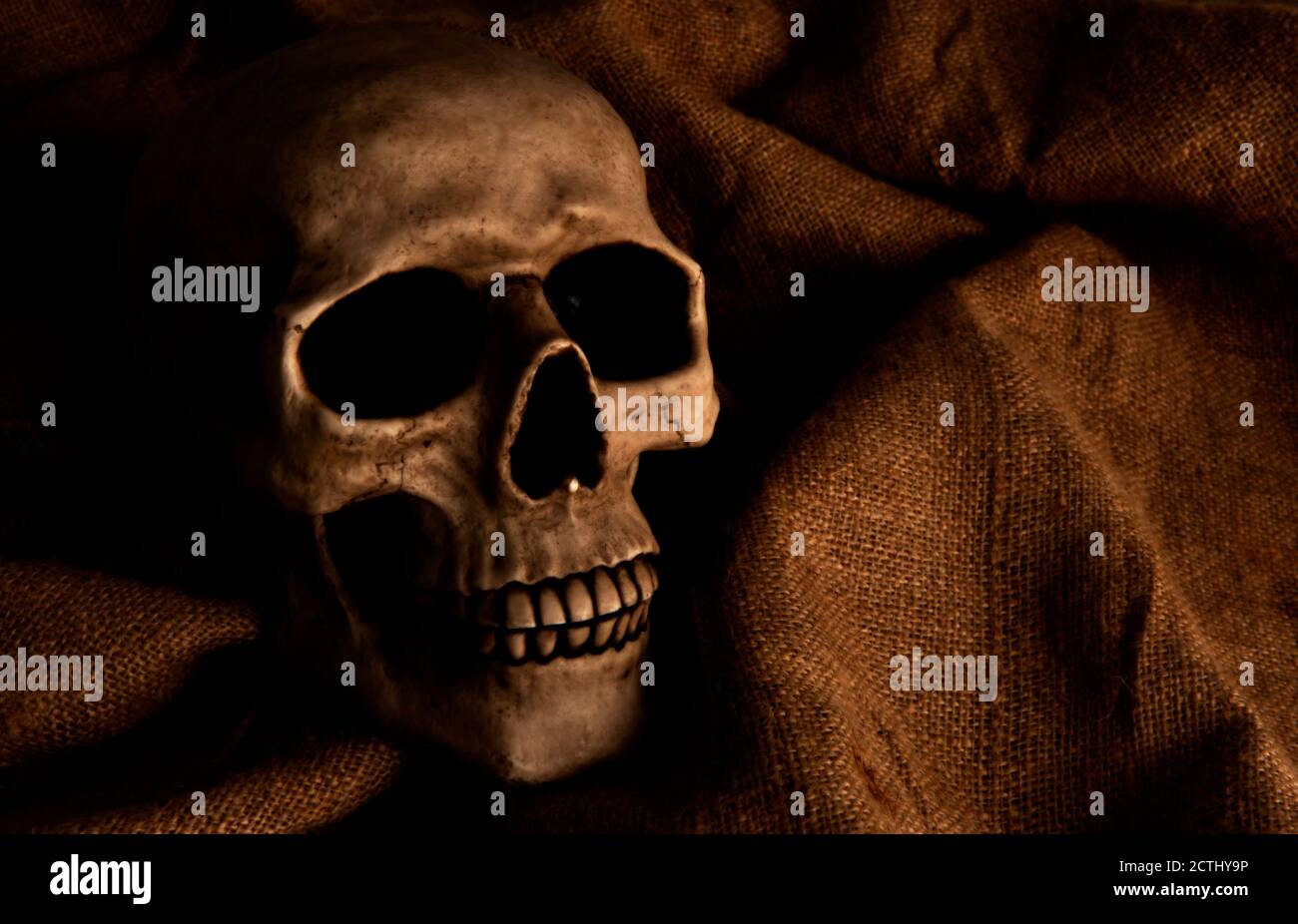 Scary dimly lit human skull laying on the gunny cloth Stock Photo