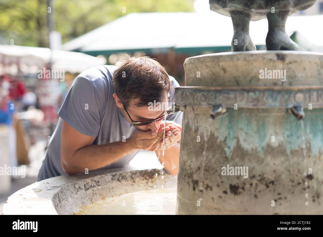 Thirsty young casual cucasian man drinking water from public city fountain on a hot summer day Stock Photo