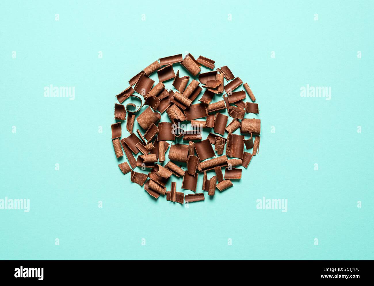 Chocolate shavings, circle shaped layout, isolated on a blue background. Top view of milk chocolate pieces. Decorative ingredients for desserts. Stock Photo
