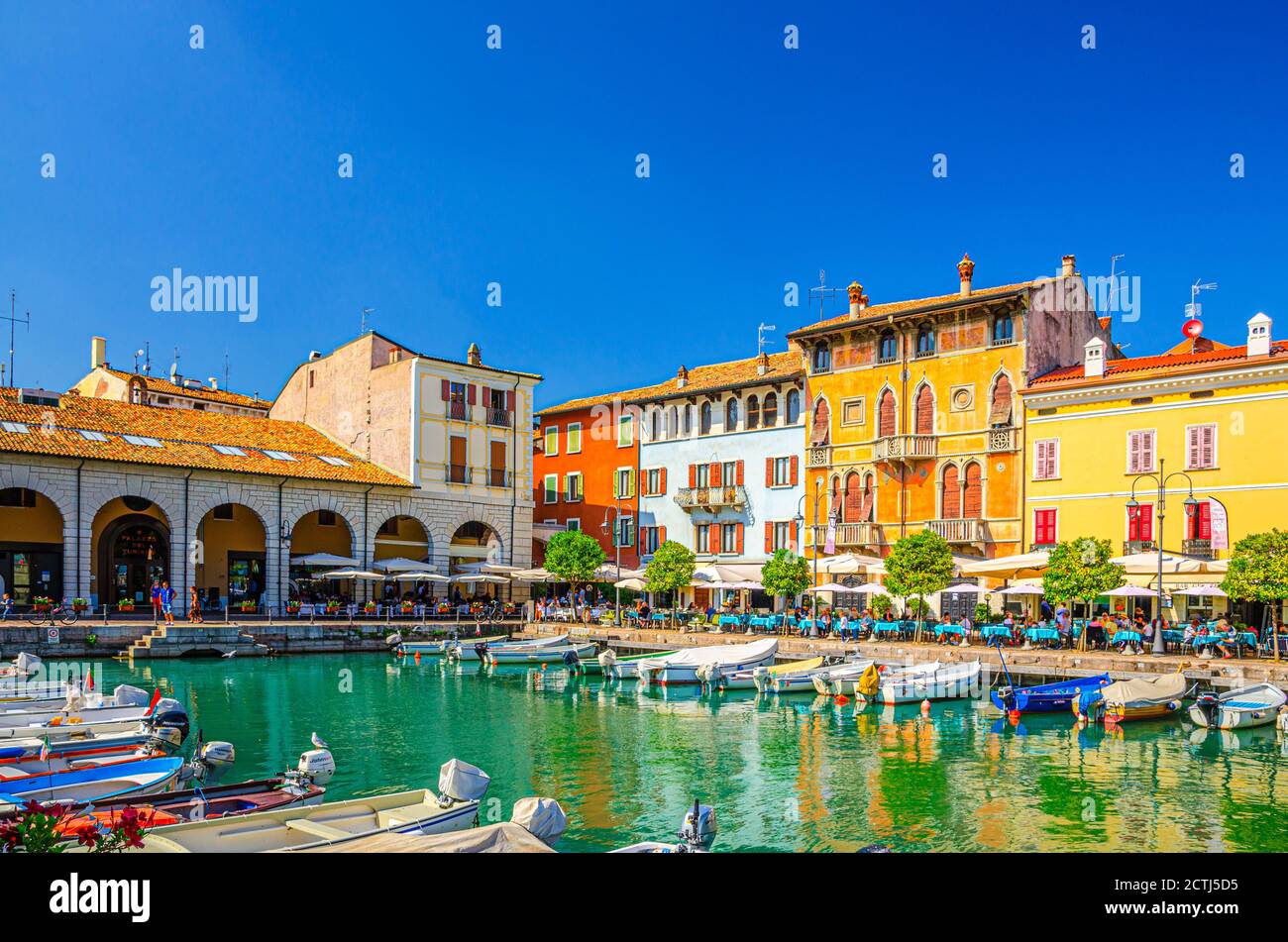 Desenzano del Garda, Italy, September 11, 2019: Old harbour Porto Vecchio with boats on turquoise water, green trees, street restaurants and traditional buildings in historical town centre, Lombardy Stock Photo