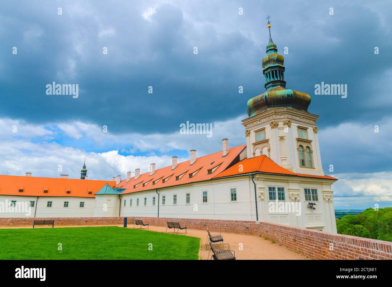 Jesuit College building, green grass lawn and benches in Park GASK, Kutna Hora historical Town Centre, blue dramatic sky background, Central Bohemian Region, Czech Republic Stock Photo