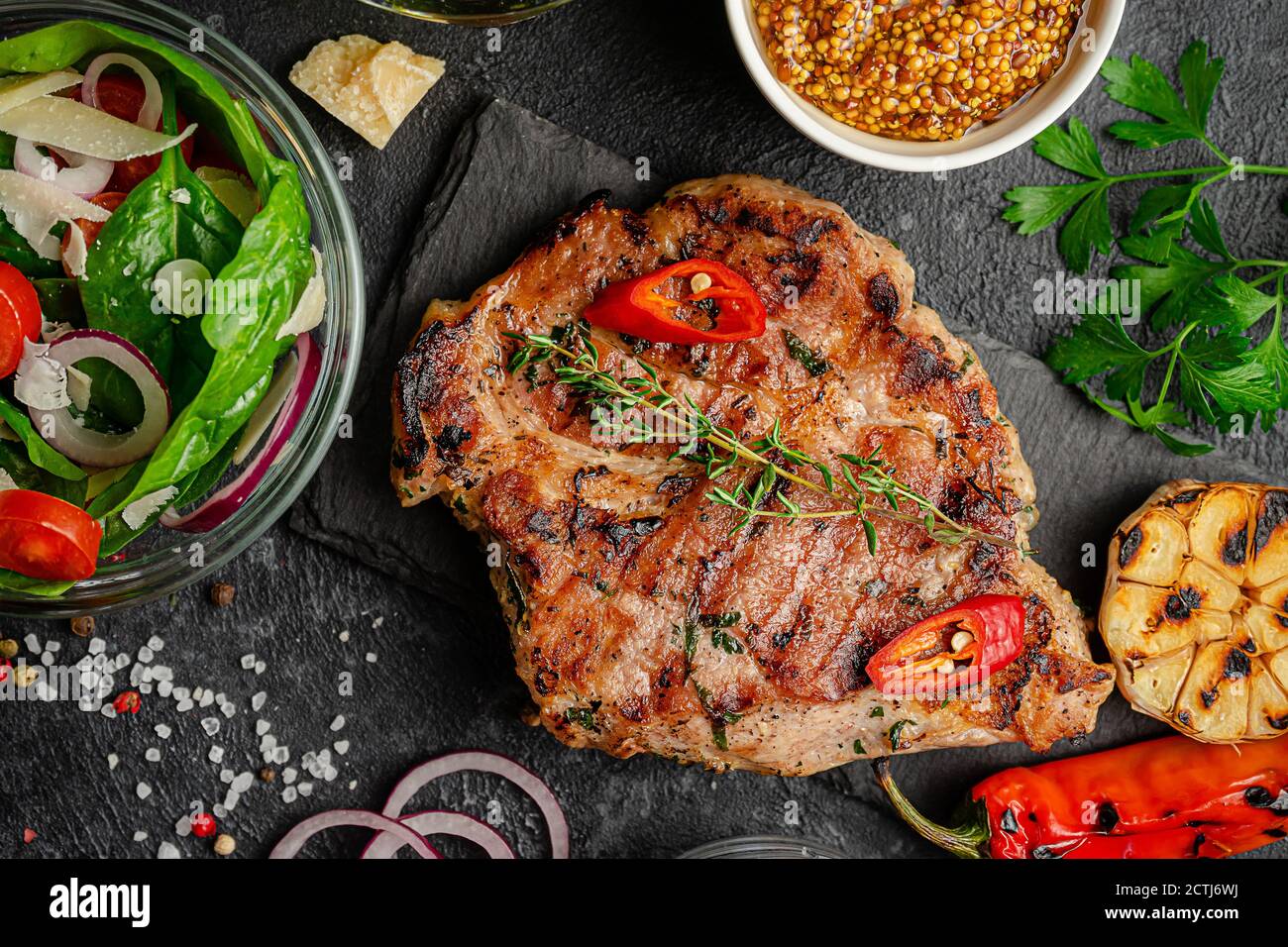 grilled-pork-steak-with-vegetables-and-fresh-salad-on-dark-background