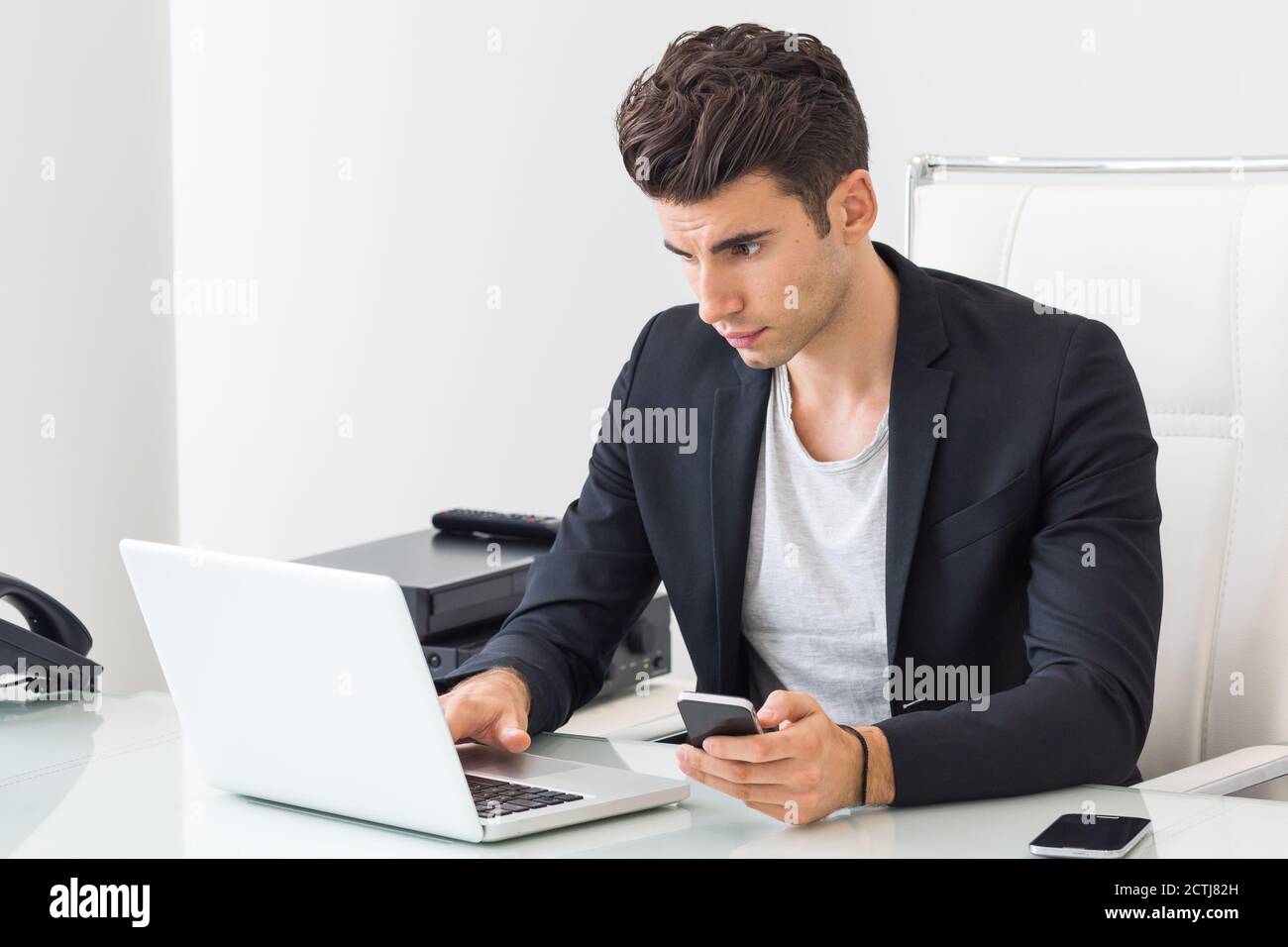 Focused businessman using a laptop computer and mobile phone at work. Stock Photo