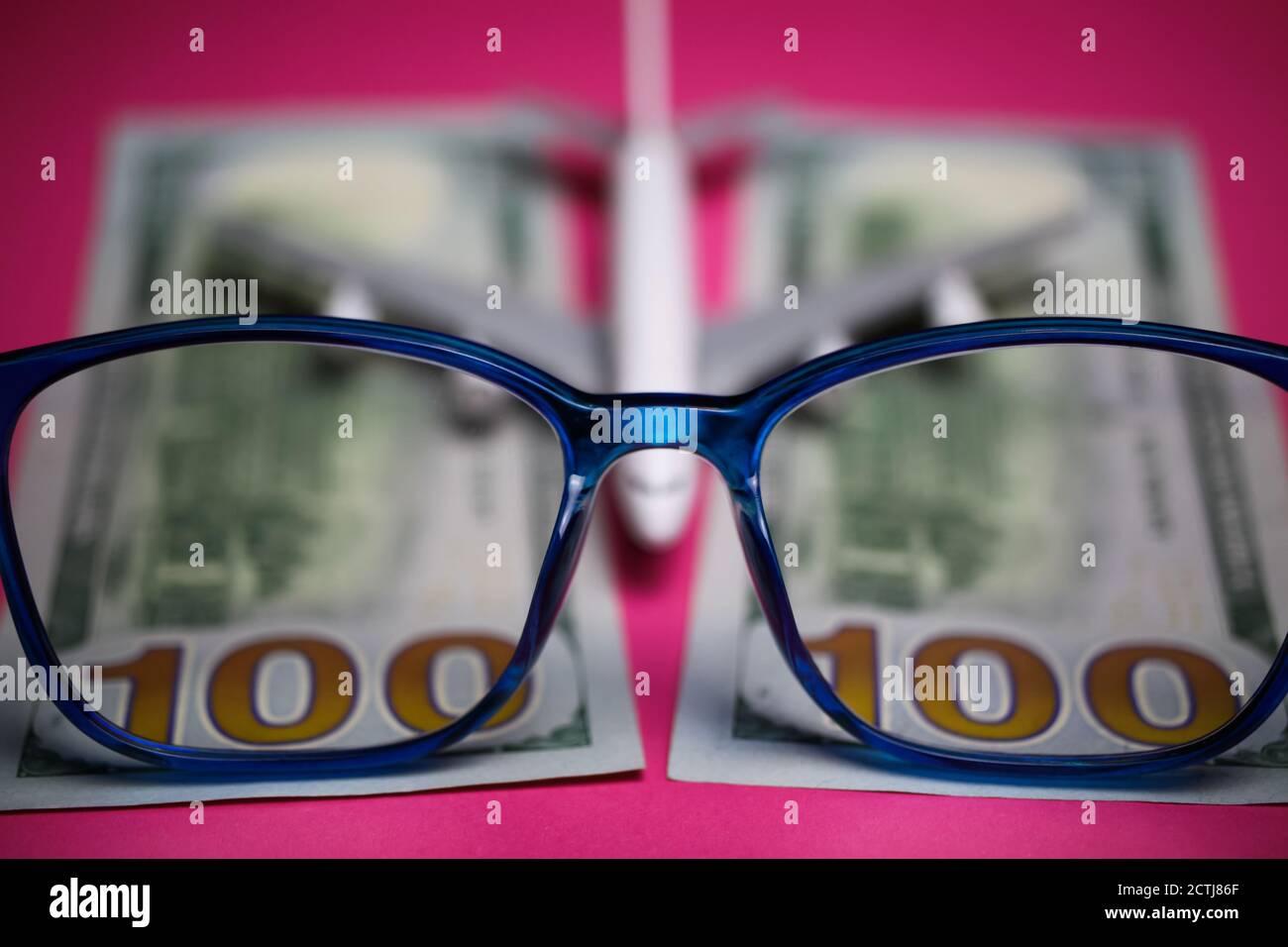 View on isolated eyeglasses with blurred plane and two hundred dollar paper banknotes on pink backgound (focus on center of eyeglass frame) Stock Photo