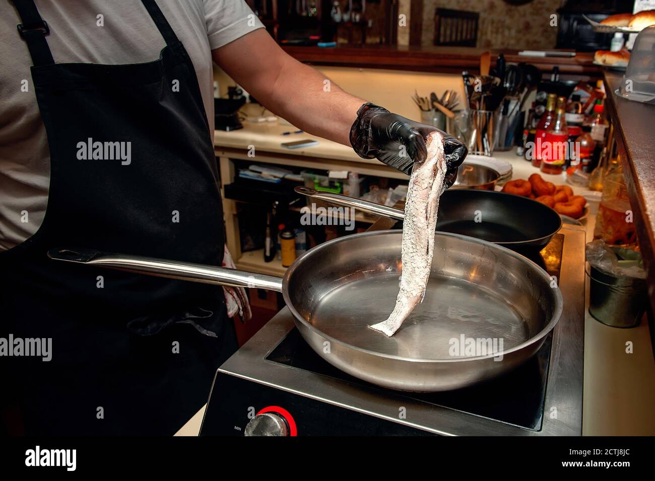 chef is frying mullet in a frying pan on an electric stove. Cooking