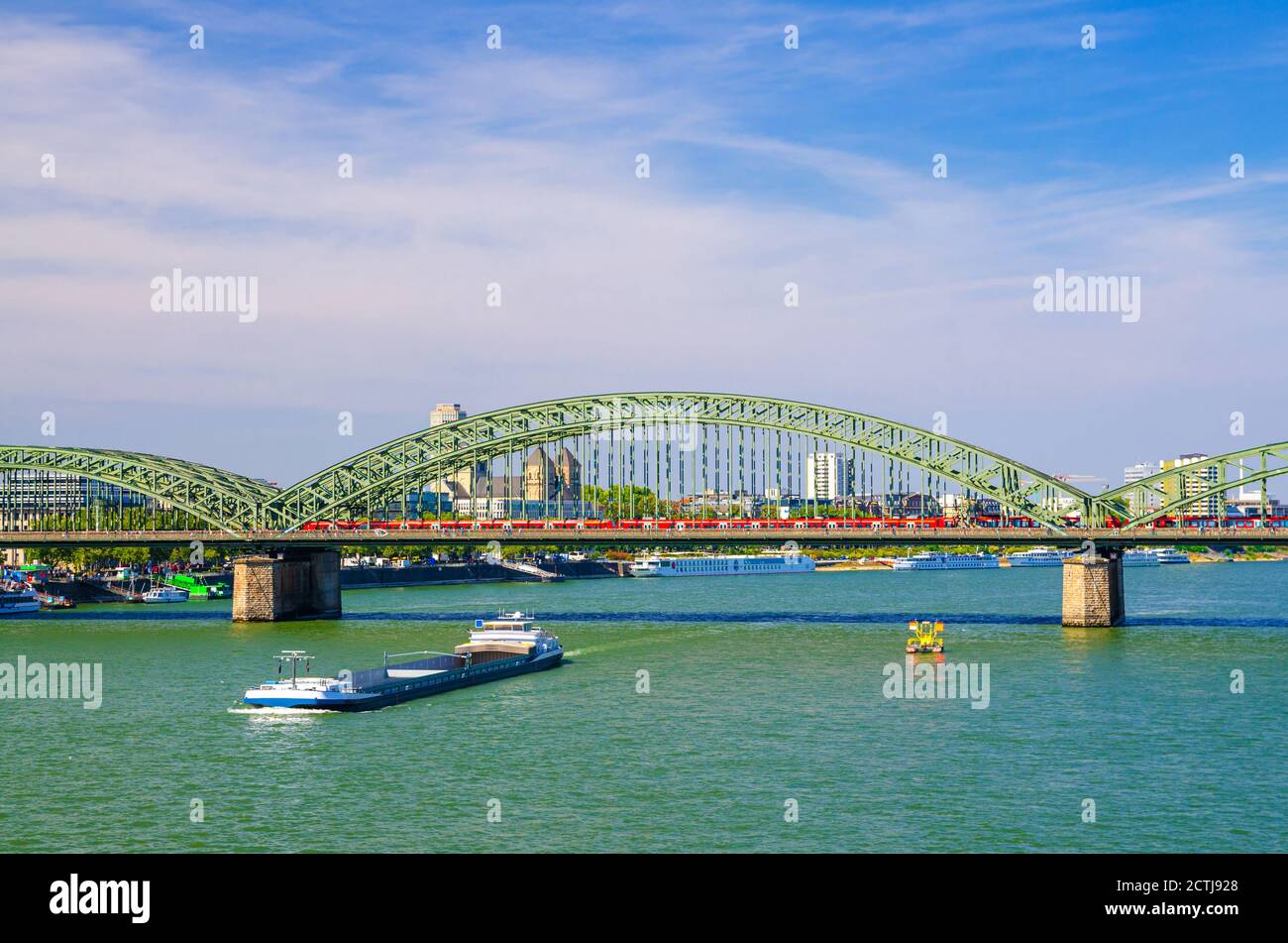 The Hohenzollern Bridge or Hohenzollernbrucke across Rhine river with cargo ships sailing on water, pedestrian and railway steel bridge, Cologne city centre, North Rhine-Westphalia, Germany Stock Photo