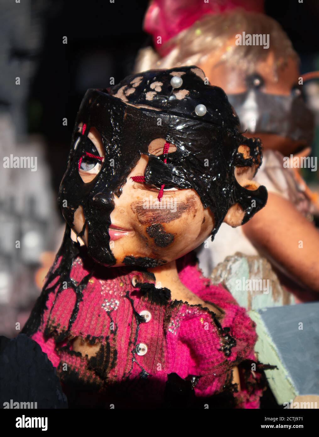 Creepy baby doll. Outside Halloween decoration. Head shot of doll with eyes stitched close and black mask. Stock Photo