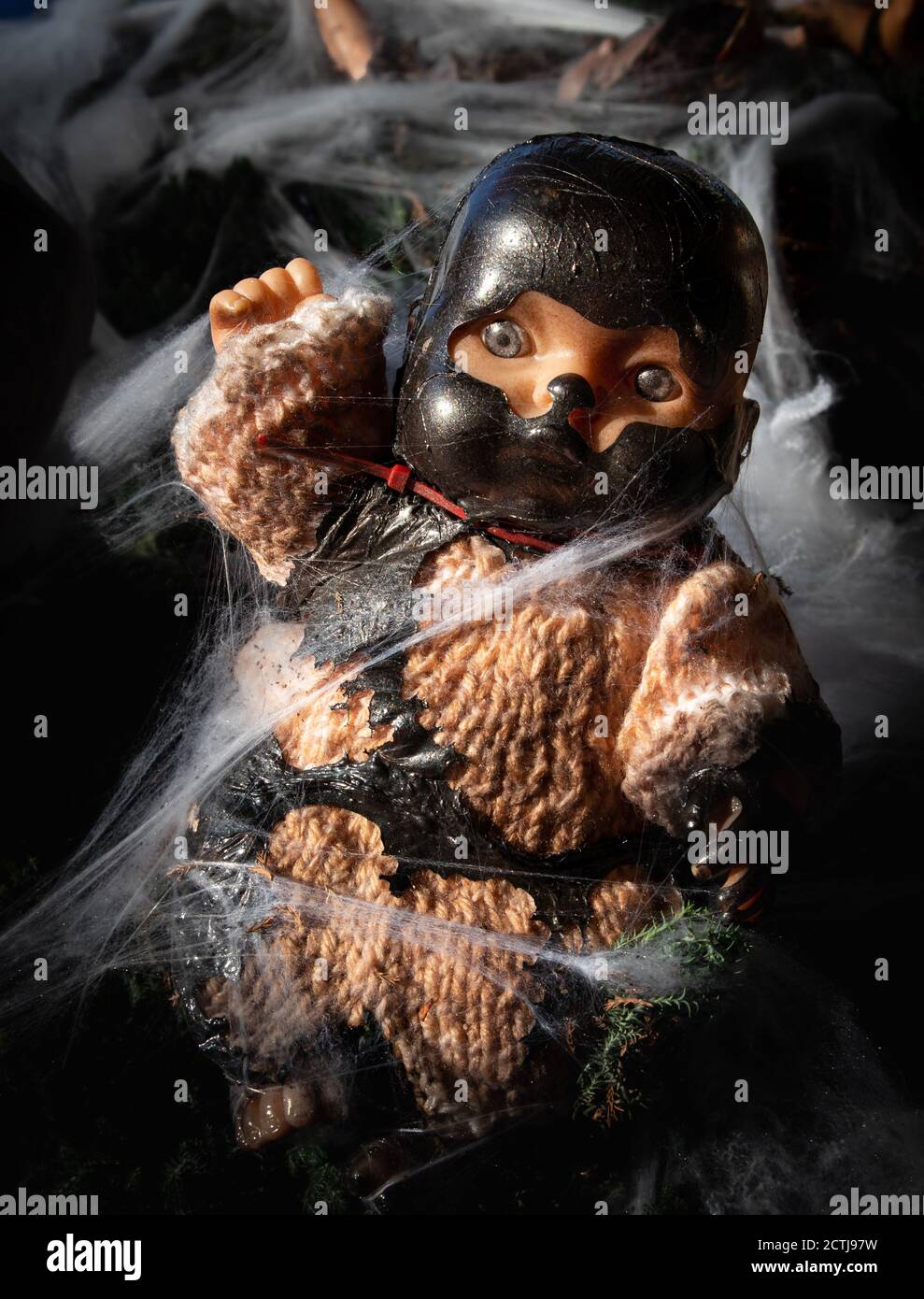 Creepy doll. Halloween decoration. The baby doll is caught in spider webs and is wearing a dark mask. Horror concept. Stock Photo