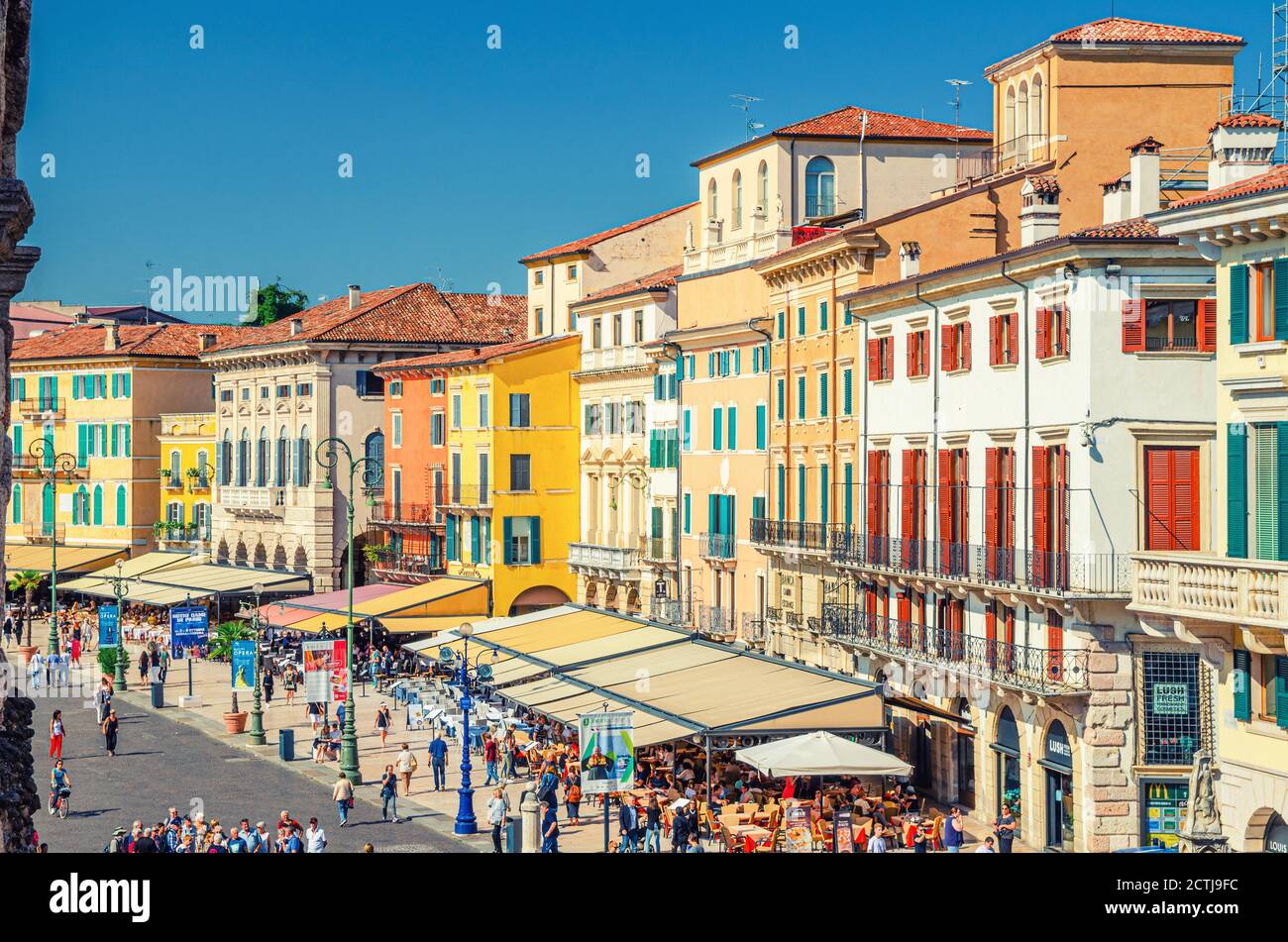 Verona, Italy, September 12, 2019: Row of old colorful multicolored buildings on Piazza Bra square in historical city centre, cafes and restaurants with tents and walking tourists, aerial view Stock Photo