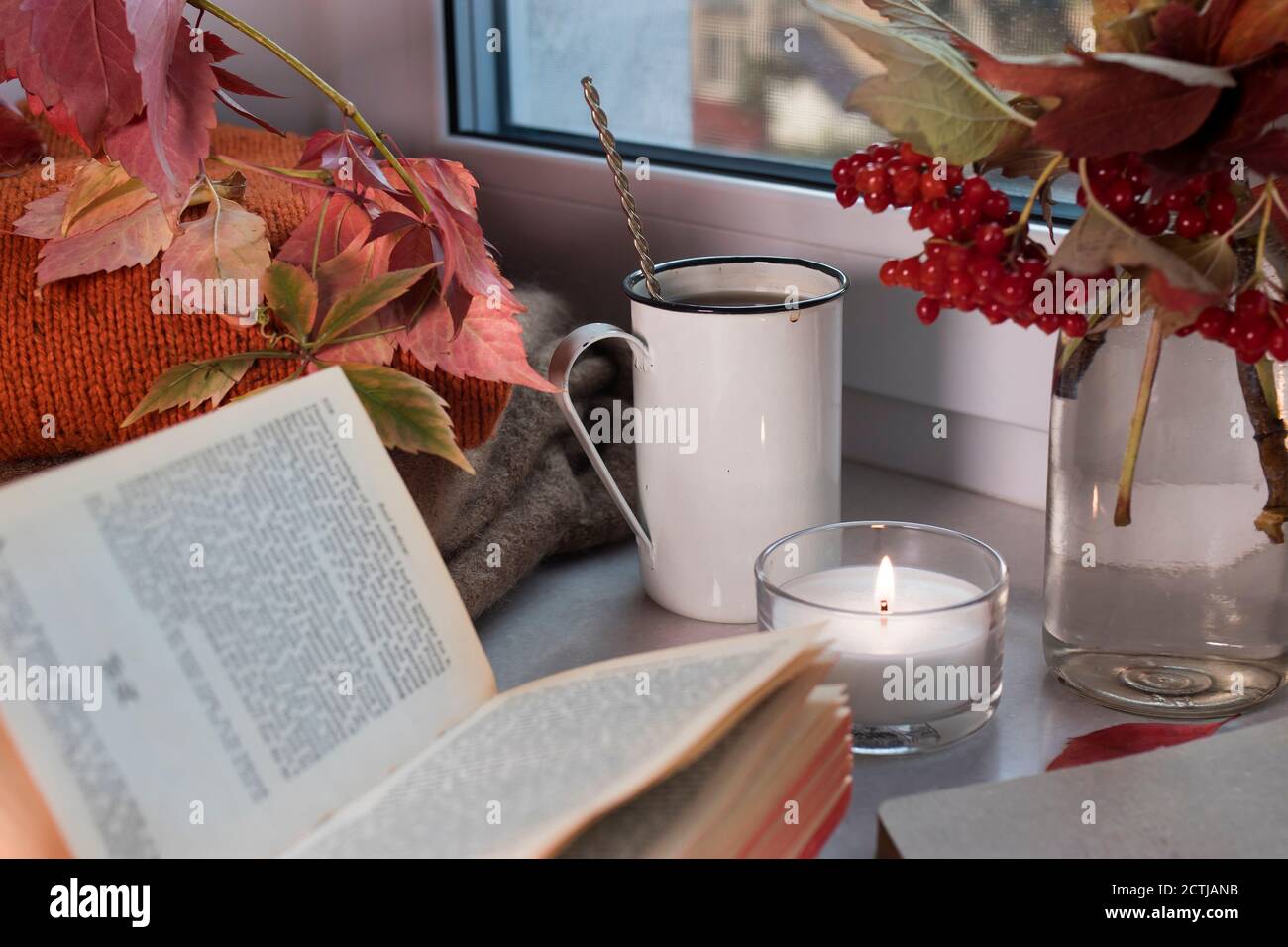 An iron cup of coffee with a spoon on the windowsill among a vase with ...