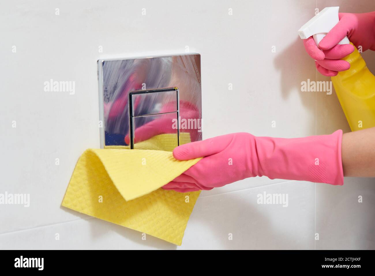Hands wearing rubber protective gloves cleaning toilet flush button