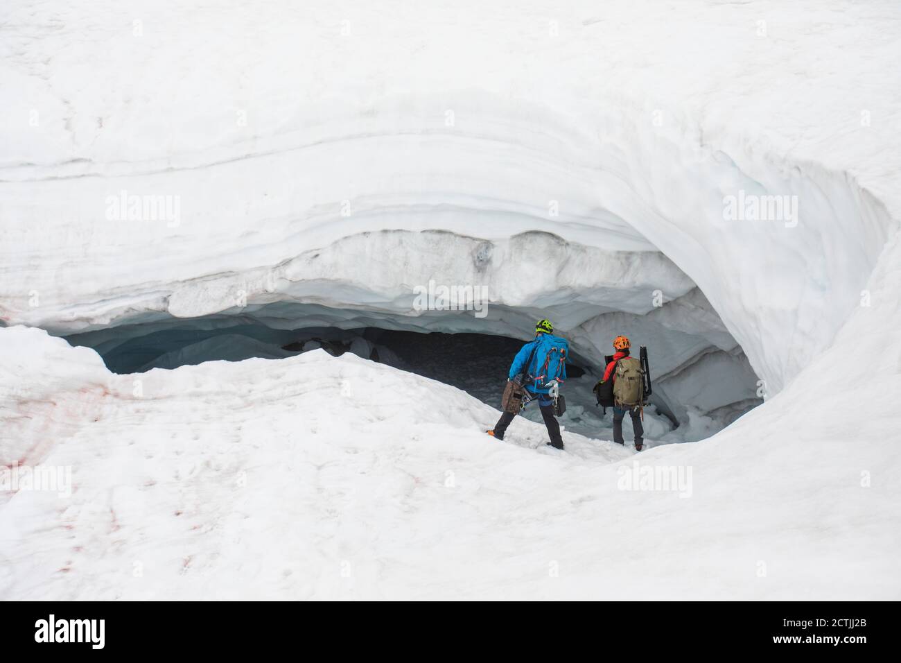 Two explorers enter the mouth of a glacial cave with gear in hand. Stock Photo